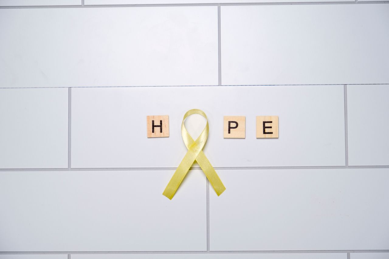 Home A yellow ribbon forming the word 'hope' with tiles on a white tiled background, symbolizing awareness and support.